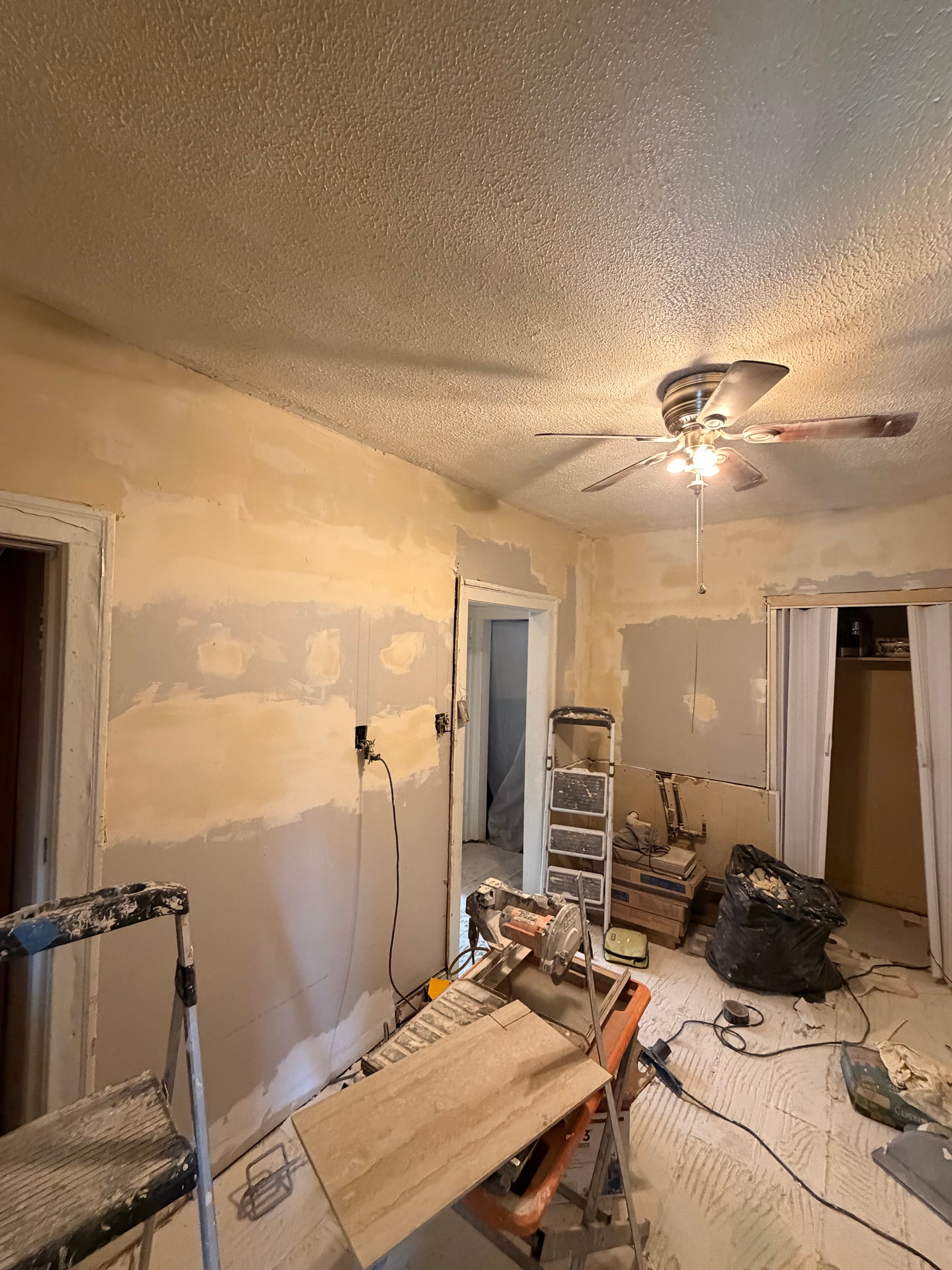 Interior room renovation with patched drywall, a tile saw, ladders, and construction debris.