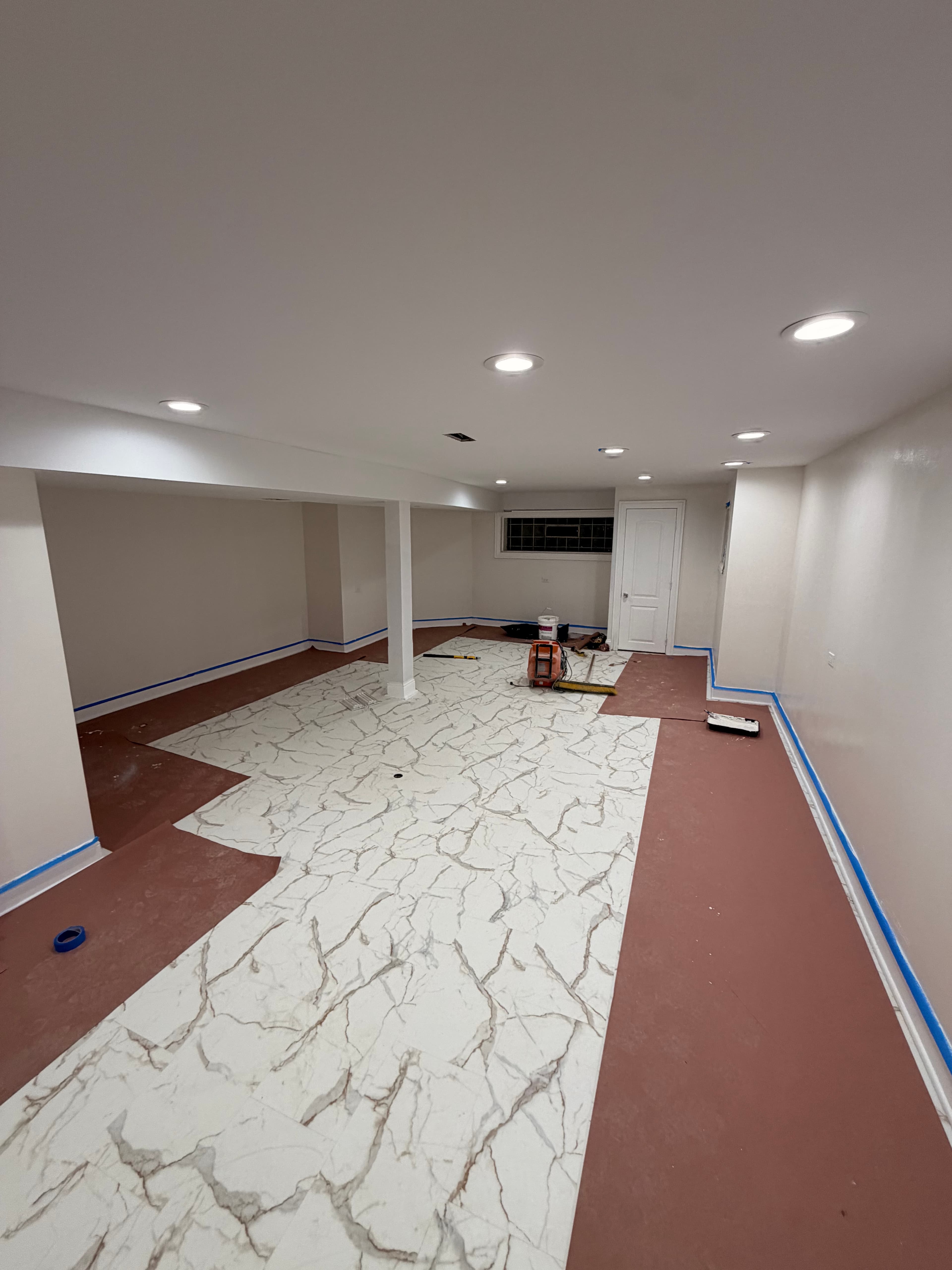 White marble patterned tiles being installed in a room with white walls and recessed lighting.