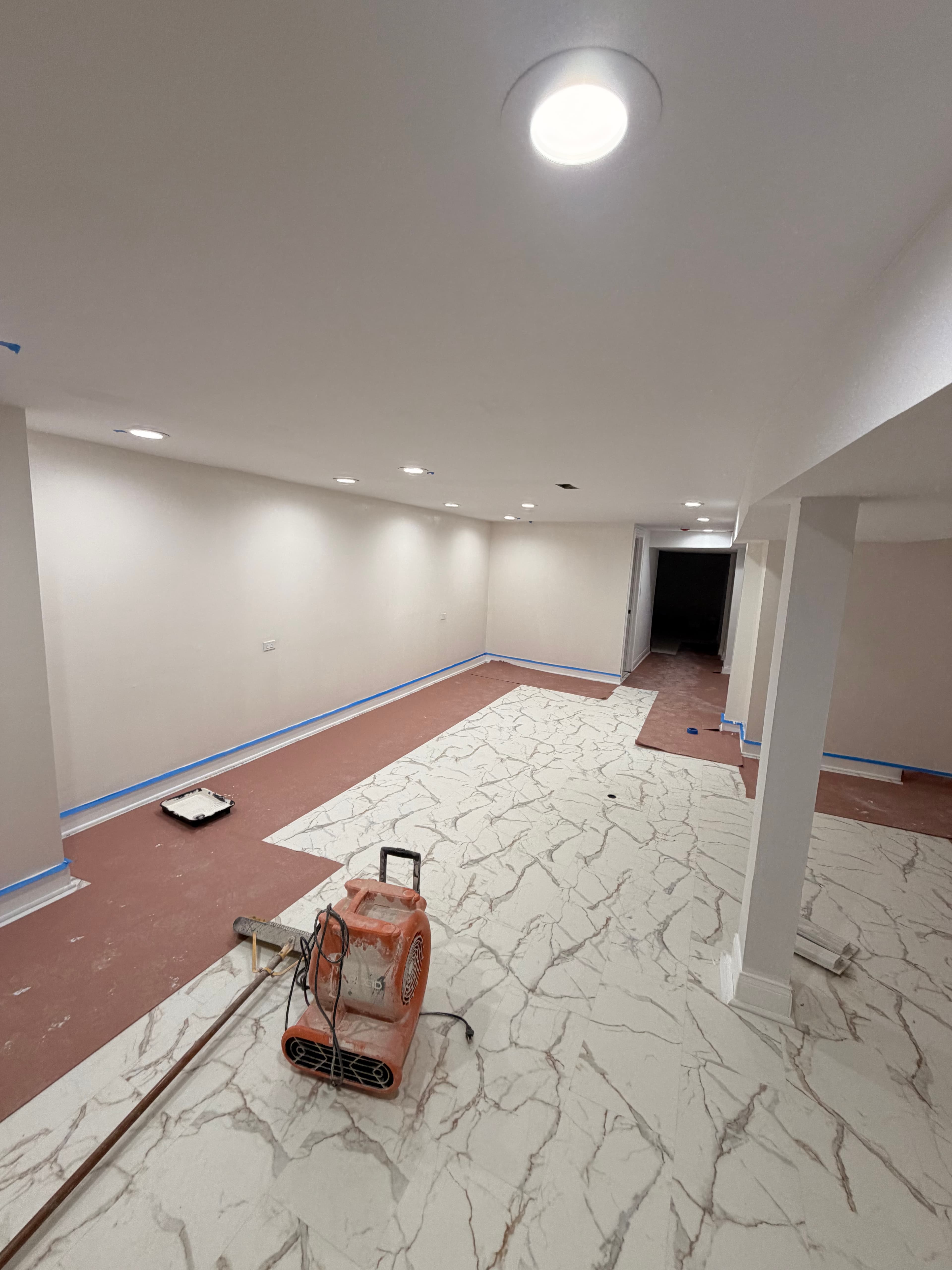 Basement renovation featuring white marble floor tiles, cream walls, and an industrial air mover.