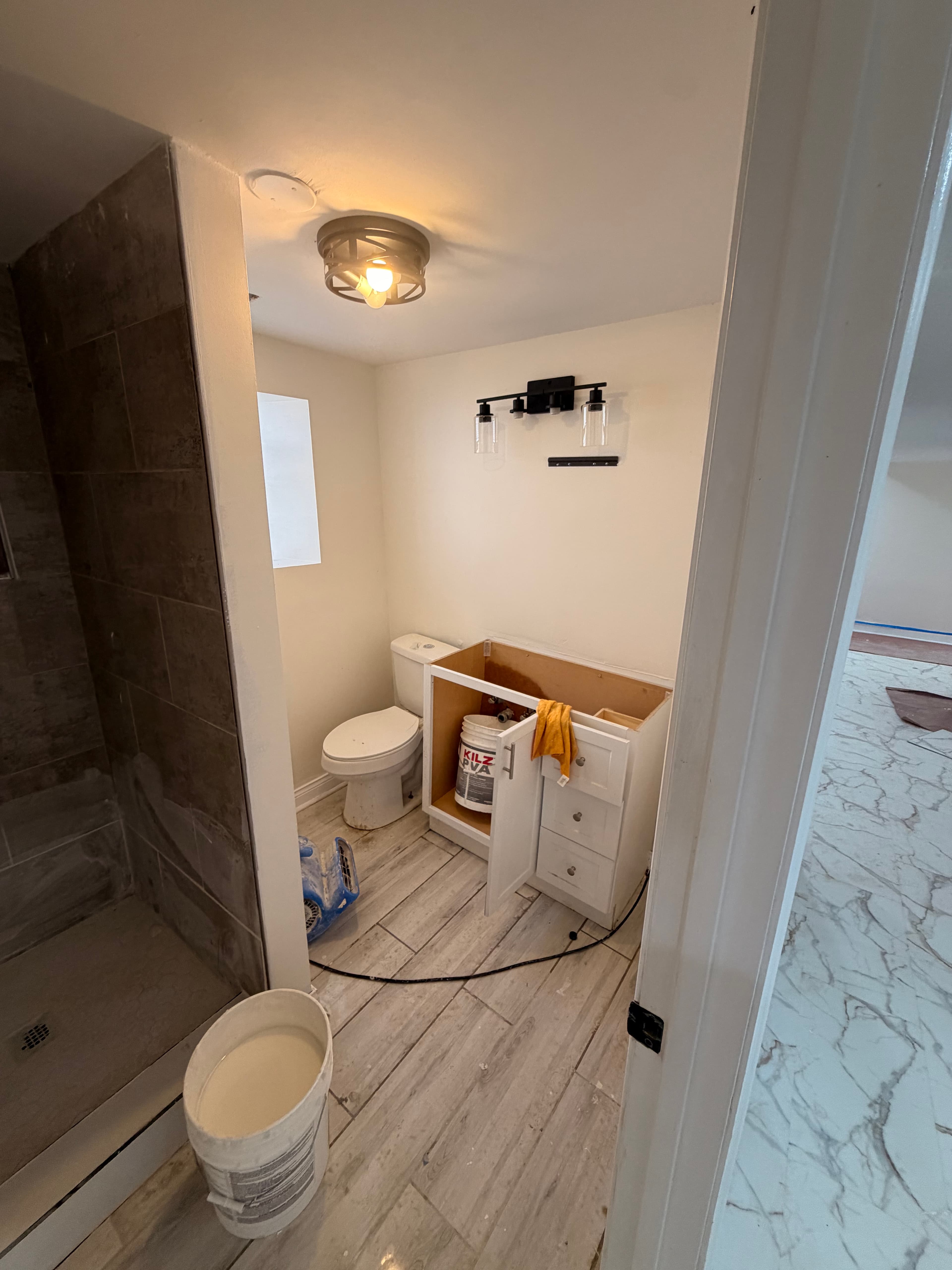 Bathroom renovation featuring a white toilet, unfinished vanity, tiled shower, and wood-look tile floors.